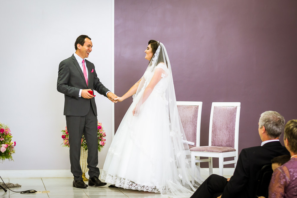 Foto da cerimônia de casamento no Salão do Reino das Testemunhas de Jeová, JW, em Santa Maria, RS. O noivo segura na mão da noiva para troca das alianças de casamento.