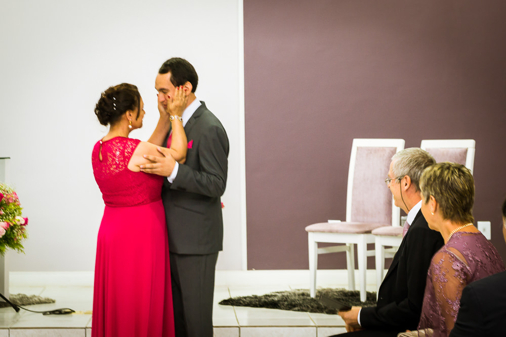 Foto da cerimônia de casamento no Salão do Reino das Testemunhas de Jeová, JW, em Santa Maria, RS. O noivo de terno, gravata e lenço com a mãe do noivo de vestido longo vermelho.