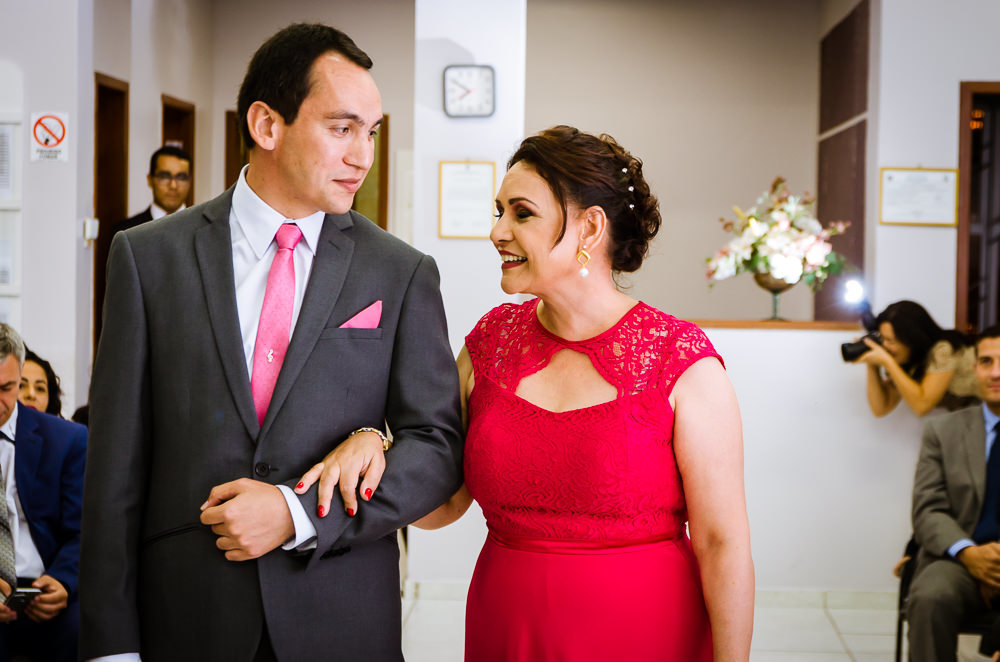 Foto da cerimônia de casamento no Salão do Reino das Testemunhas de Jeová, JW, em Santa Maria, RS. O noivo de terno, gravata e lenço com a mãe do noivo de vestido longo vermelho.