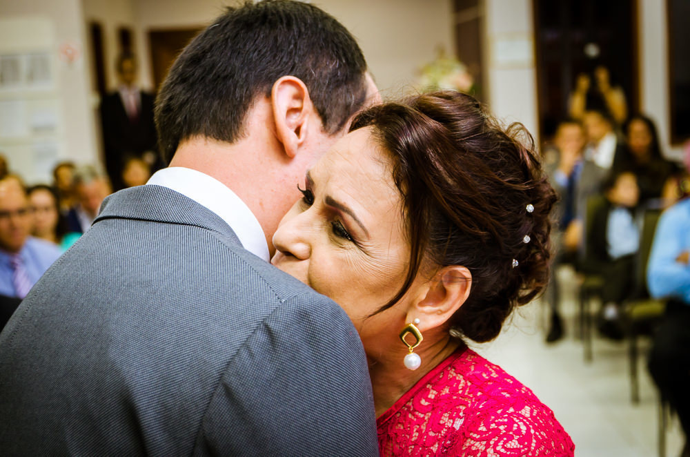Foto da cerimônia de casamento no Salão do Reino das Testemunhas de Jeová, JW, em Santa Maria, RS. O noivo de terno, gravata e lenço com a mãe do noivo de vestido longo vermelho.