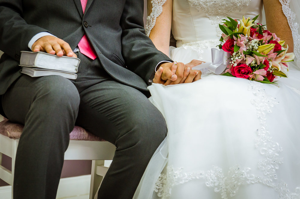 Foto da cerimônia de casamento no Salão do Reino das Testemunhas de Jeová, JW, em Santa Maria, RS. Noivos sentados no discurso de casamento de mãos dadas e Bíblia na mão do noivo.