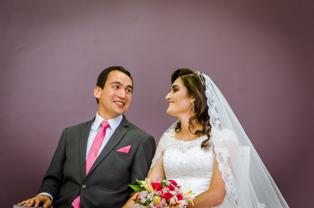 Foto da cerimônia de casamento no Salão do Reino das Testemunhas de Jeová, JW, em Santa Maria, RS. Noivos se olham sorrindo com ternura.