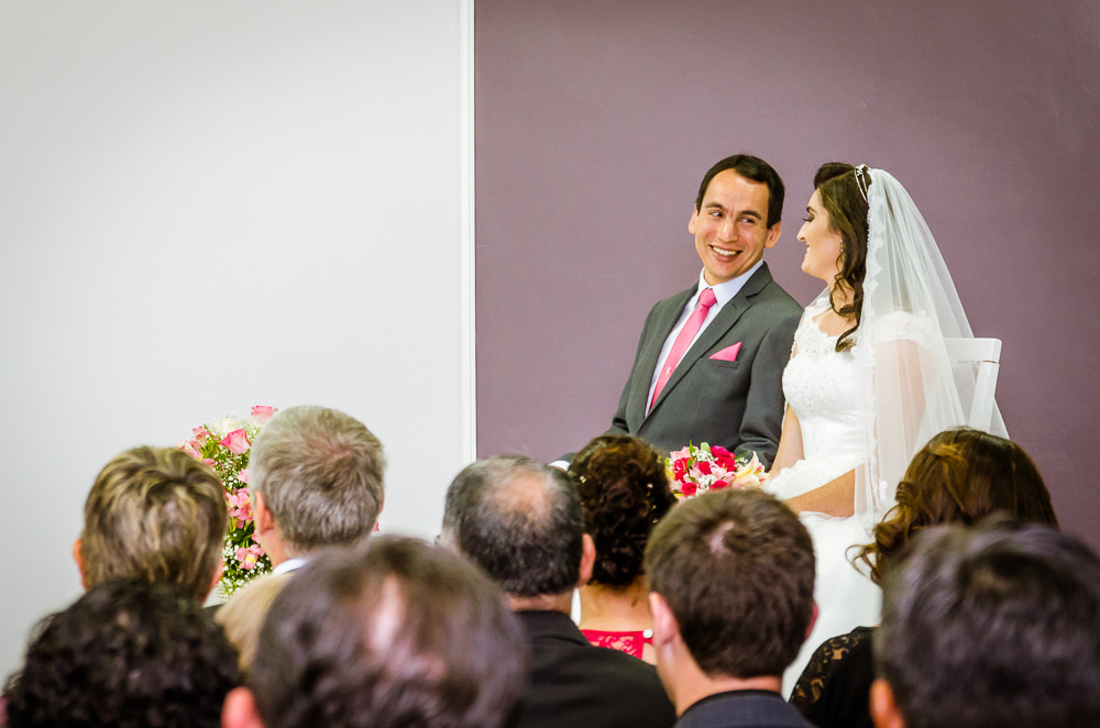 Foto da cerimônia de casamento no Salão do Reino das Testemunhas de Jeová, JW, em Santa Maria, RS. Orador do discurso de casamento, noivos sentados se olhando e convidados no auditório.
