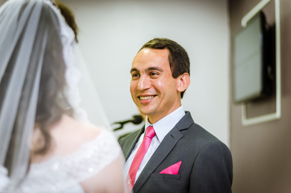 Foto da cerimônia de casamento no Salão do Reino das Testemunhas de Jeová, JW, em Santa Maria, RS. Noivo ouve os votos de casamento da noiva e sorri com ternura.