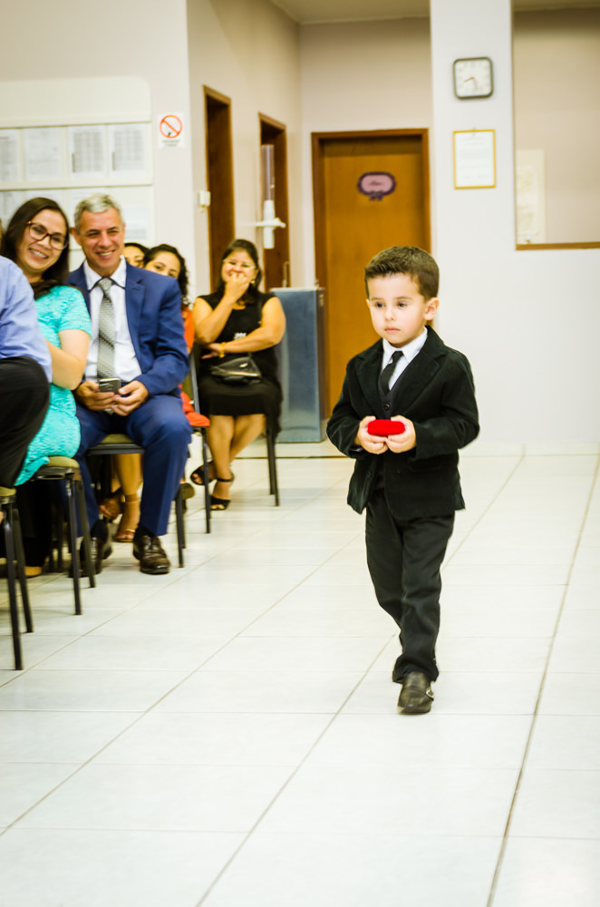Foto da cerimônia de casamento no Salão do Reino das Testemunhas de Jeová, JW, em Santa Maria, RS. Junto com os convidados uma criança de terno e grava leva as alianças para o casal de noivos.