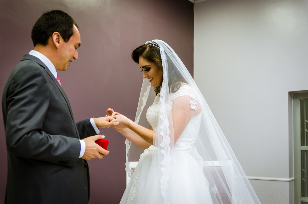 Foto da cerimônia de casamento no Salão do Reino das Testemunhas de Jeová, JW, em Santa Maria, RS. Noiva coloca a aliança na mão do noivo.