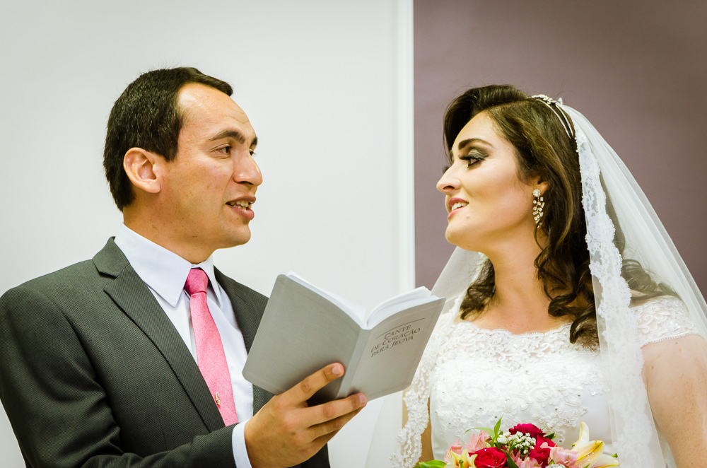 Foto da cerimônia de casamento no Salão do Reino das Testemunhas de Jeová, JW, em Santa Maria, RS. O noivo e a noiva cantam juntos e se olham com ternura.