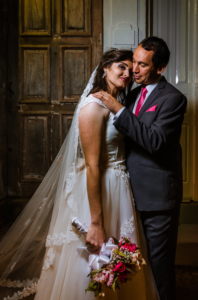 Foto do retrato no ensaio fotográfico no dia do casamento dos noivos. Ele de terno, gravata e ela de vestido de noiva branco, na Vila Belga em Santa Maria, RS