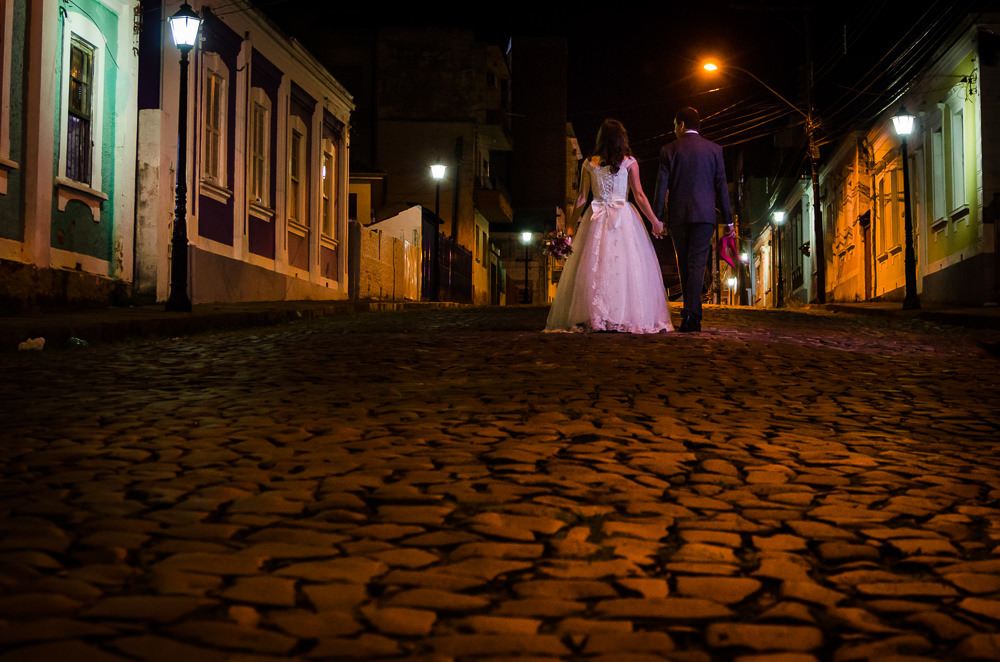 Foto do retrato no ensaio fotográfico no dia do casamento dos noivos. Ele de terno, gravata e ela de vestido de noiva branco, na Vila Belga em Santa Maria, RS
