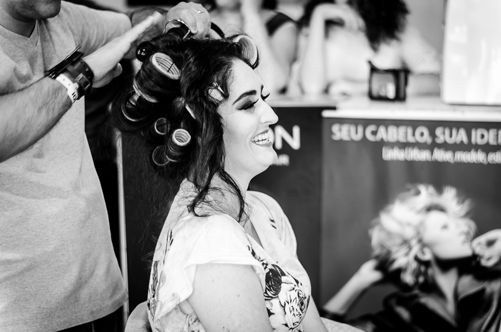 Foto do ensaio making ok na noiva no salão de beleza Centher Hair no dia da noiva fazendo o penteado e maquiagem. Ela sorri enquanto o cabeleireiro faz o penteado. Em Santa Maria, RS