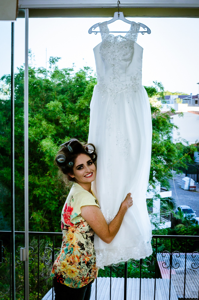 Foto do ensaio making ok na noiva no salão de beleza Centher Hair no dia da noiva fazendo o penteado e maquiagem. A noiva sorri e abraço o vestido de noiva brando e longo. Em Santa Maria, RS