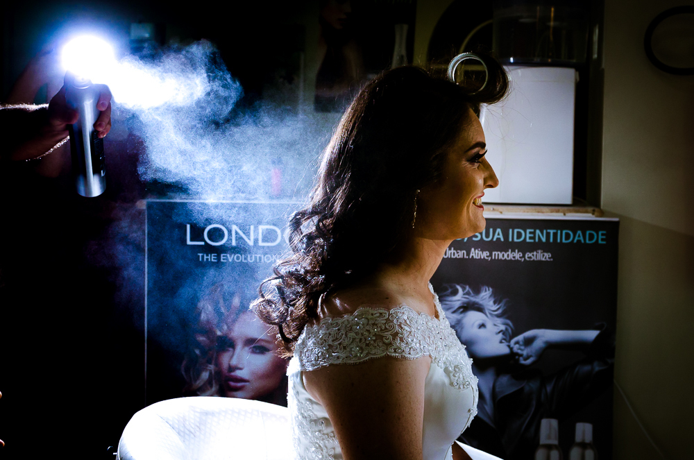 Foto do ensaio making ok na noiva no salão de beleza Centher Hair no dia da noiva fazendo o penteado e maquiagem. Ela sorri enquanto o cabeleireiro faz o penteado. Em Santa Maria, RS