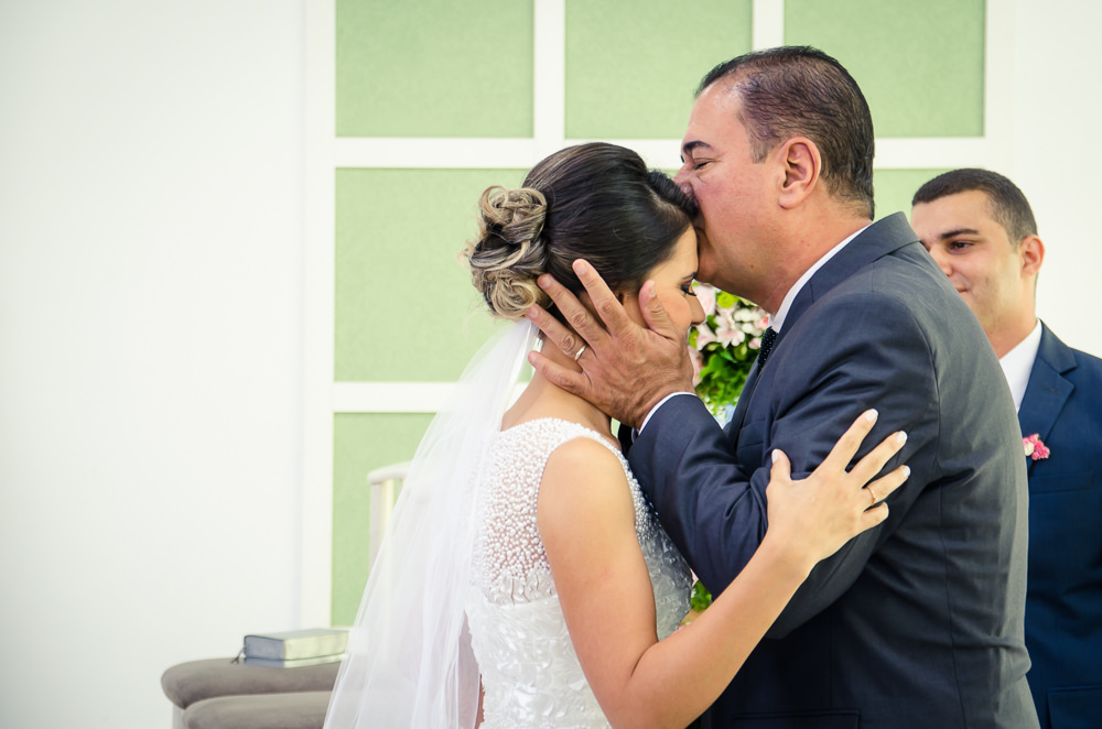 Fotografia da noiva de vestido branco na entrada da noiva para cerimônia de casamento com o pai que beija a testa da noiva em Cajamar, São Paulo