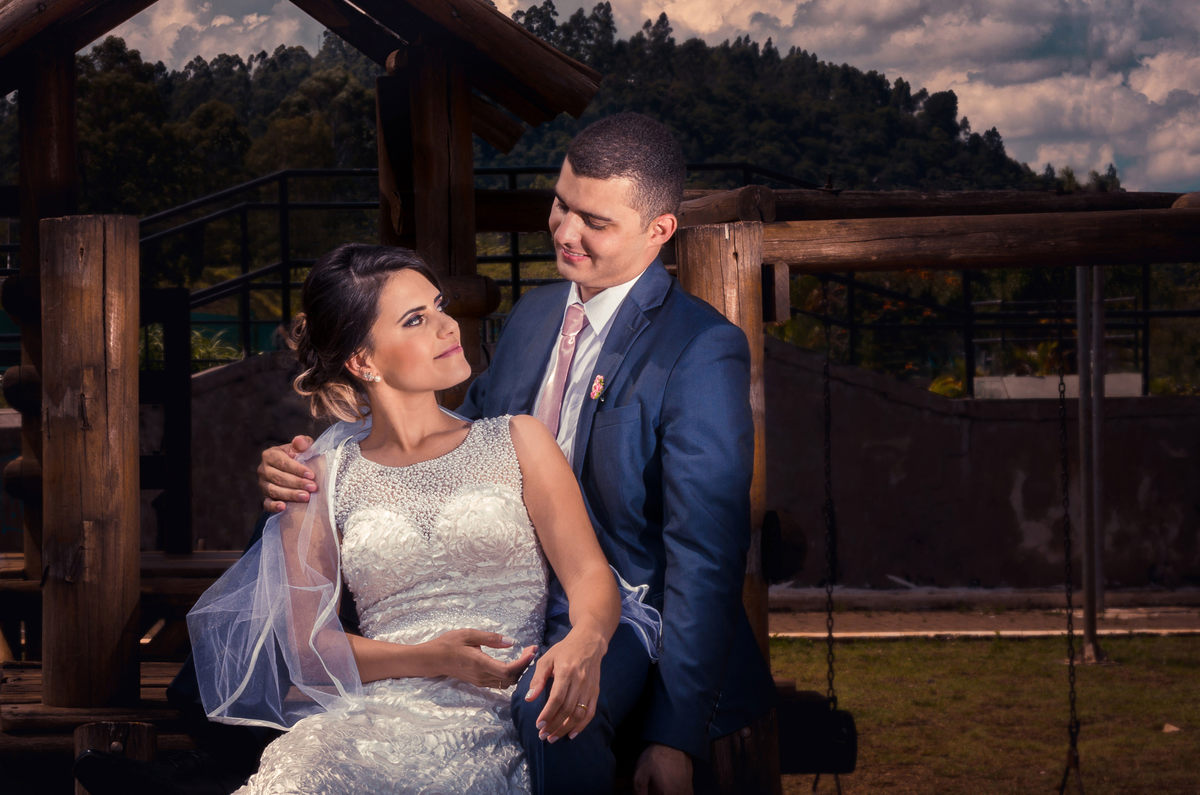 Foto do ensaio após a cerimônia de casamento dos noivos. A noiva está de vestido de noiva branco e véu e o noivo de terno azul e gravata rosa em Cajamar, São Paulo