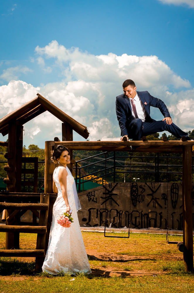 Foto do ensaio após a cerimônia de casamento dos noivos. A noiva está de vestido de noiva branco e véu com o bouquet, buquê, e o noivo de terno azul e gravata rosa em Cajamar, São Paulo