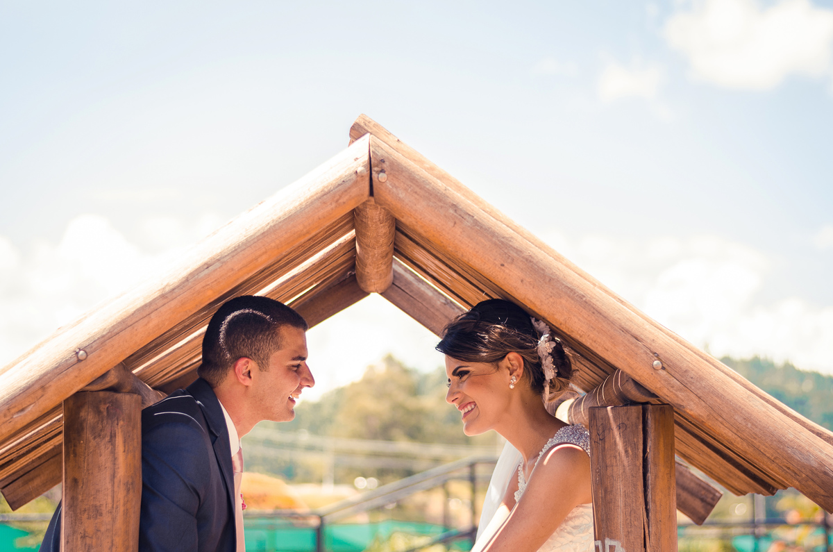 Foto do ensaio após a cerimônia de casamento dos noivos. A noiva está de vestido de noiva branco e véu com o bouquet, buquê, e o noivo de terno azul e gravata rosa em Cajamar, São Paulo