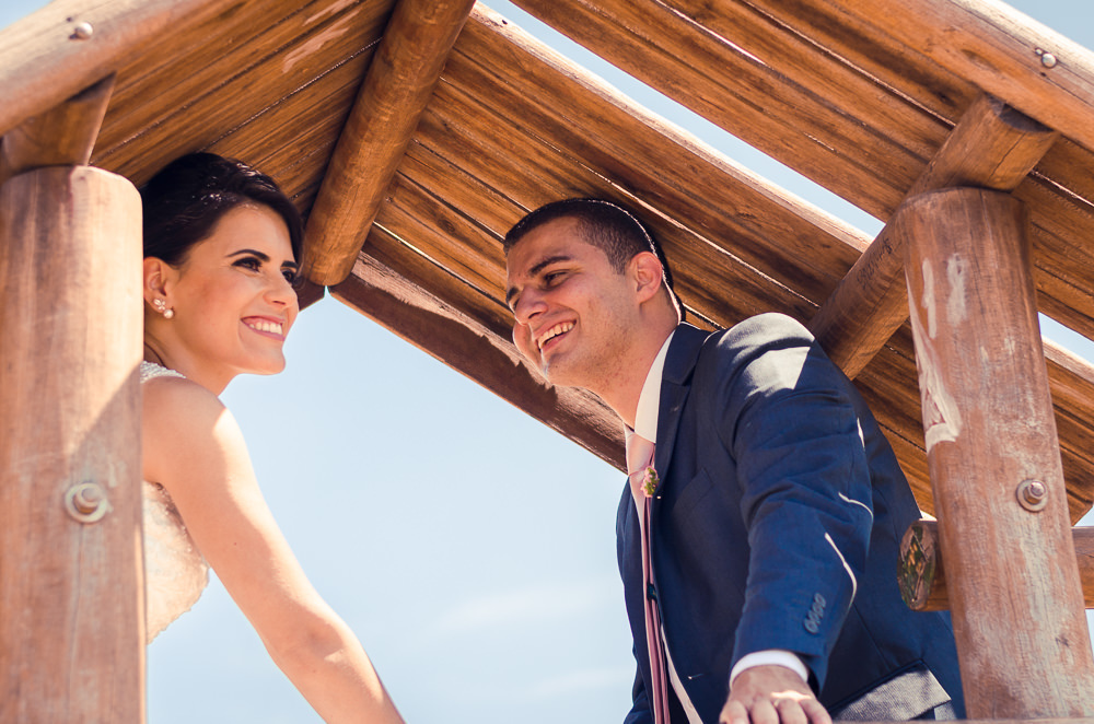 Foto do ensaio após a cerimônia de casamento dos noivos. A noiva está de vestido de noiva branco e véu com o bouquet, buquê, e o noivo de terno azul e gravata rosa em Cajamar, São Paulo