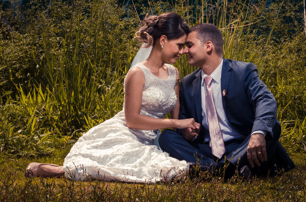 Foto do ensaio após a cerimônia de casamento dos noivos. A noiva está de vestido de noiva branco e véu com o bouquet, buquê, e o noivo de terno azul e gravata rosa em Cajamar, São Paulo