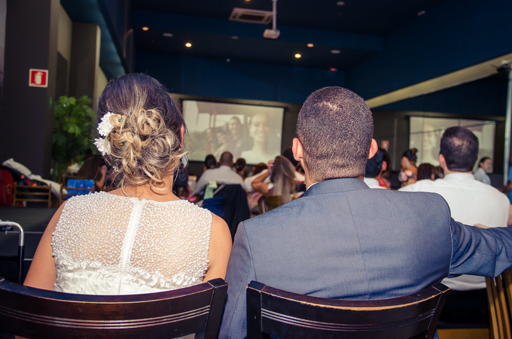 Foto dos noivos chegando a recepção por adesão no Anhanguera Parque Shopping, a noiva está de vestido brando e véu com o bouquet, buquê e o noivo de terno azul e gravata rosa em Cajamar, São Paulo