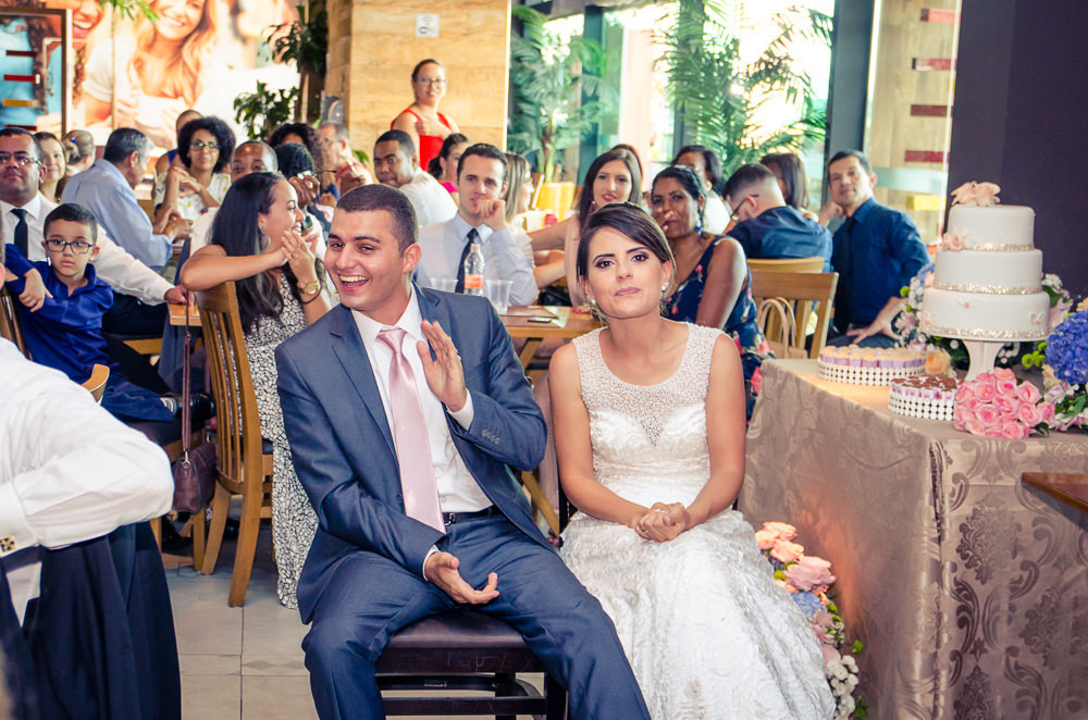 Foto dos noivos chegando a recepção por adesão no Anhanguera Parque Shopping, a noiva está de vestido brando e véu com o bouquet, buquê e o noivo de terno azul e gravata rosa em Cajamar, São Paulo