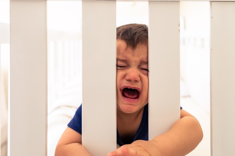 Fotografia Documental de Família. Foto da rotina da família com seu filho criança bebê, mostrando a essência a história da família.  Foto em Barueri, SP. Bebê criança dentro do berço chorando.