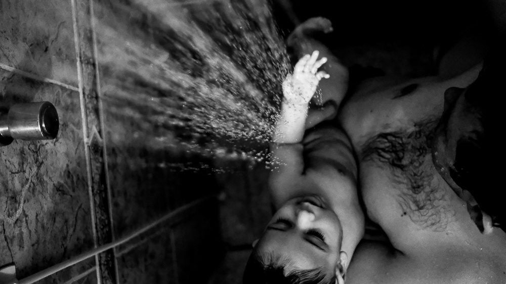 Fotografia documental de Família, Filho com o pai tomando banho no chuveiro, foto em PB, preto e Branco. Carinho do papai com o filho em Barueri, SP, São Paulo