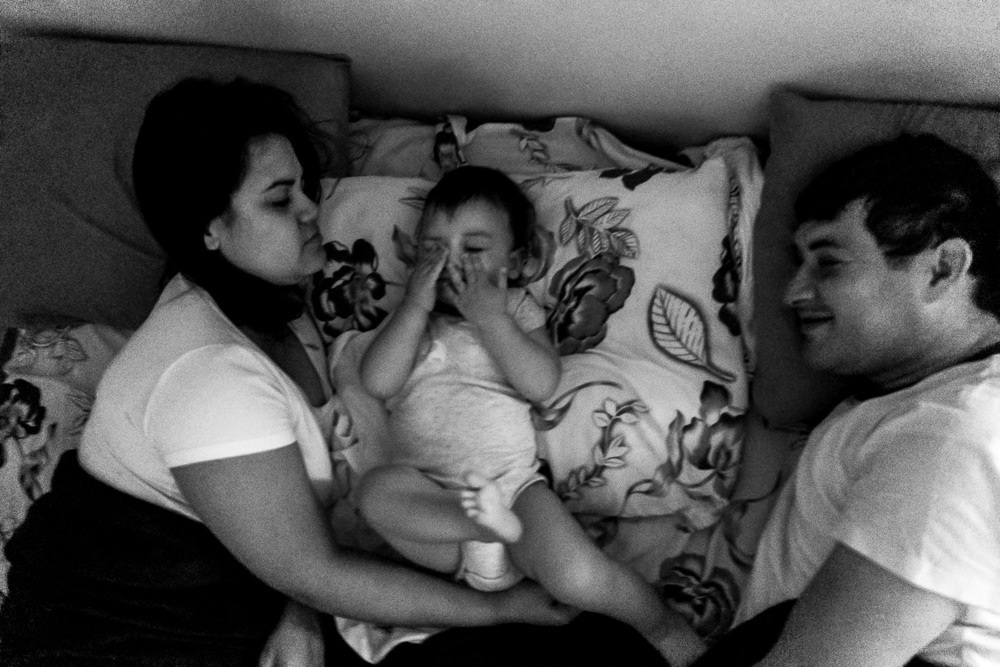 Fotografia documental de Família, Hora de acordar, pai, mãe e filho criança na cama acordando. Foto em PB preto e branco em Barueri SP