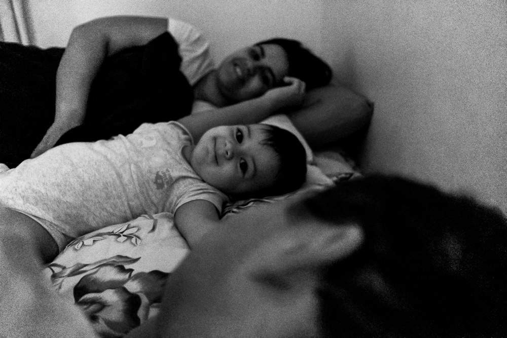 Fotografia documental de Família, Hora de acordar, pai, mãe e filho criança na cama acordando. Foto em PB preto e branco em Barueri SP