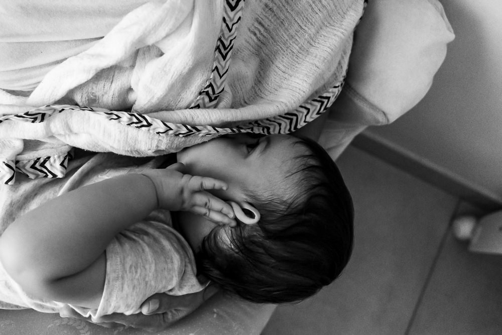 Fotografia Documental de Família. Foto da rotina da família com seu filho criança bebê, mostrando a essência a história da família.  Foto em Barueri, SP. Criança no colo da mamãe mamando no peito mexendo na orelha