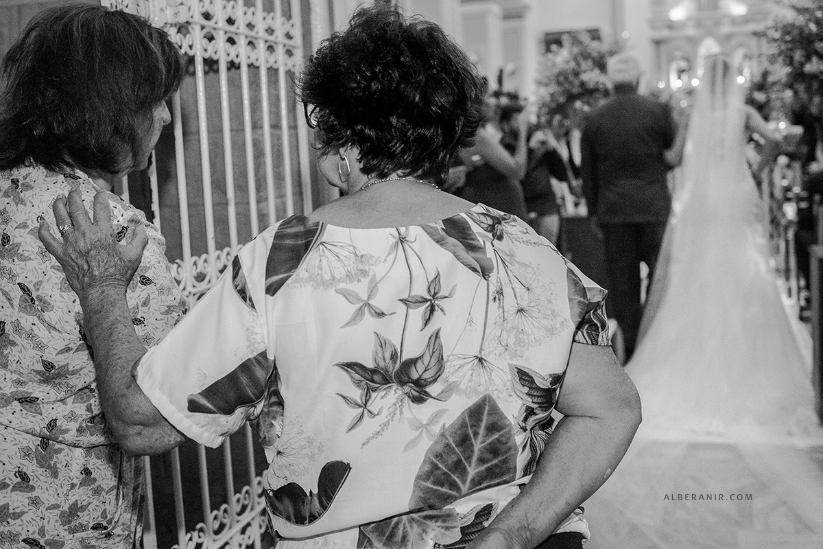 Noiva entrando na igreja. Senhorinhas observando e conversando.