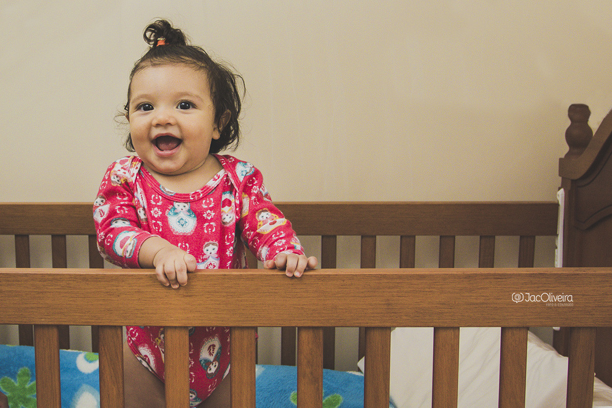 isa rindo no berço em pé no ensaio de bebê