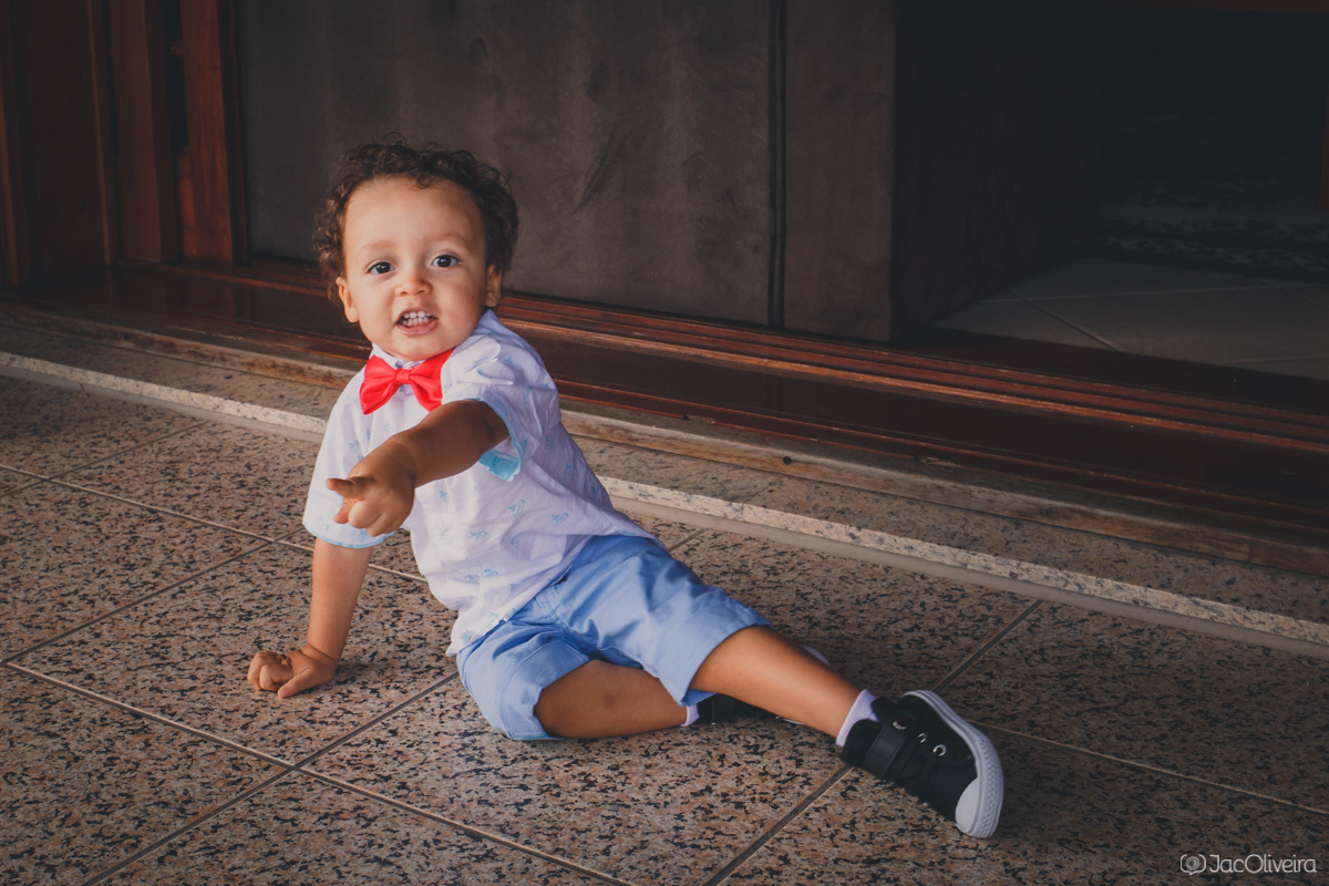 menino brinca no chão da casa da vó com tenis e gravata borboleta