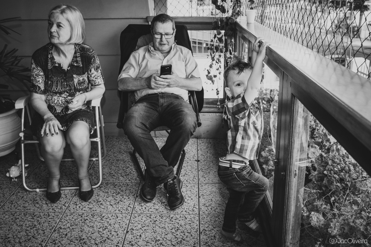 avós olham no celular enquanto neto brinca na varanda