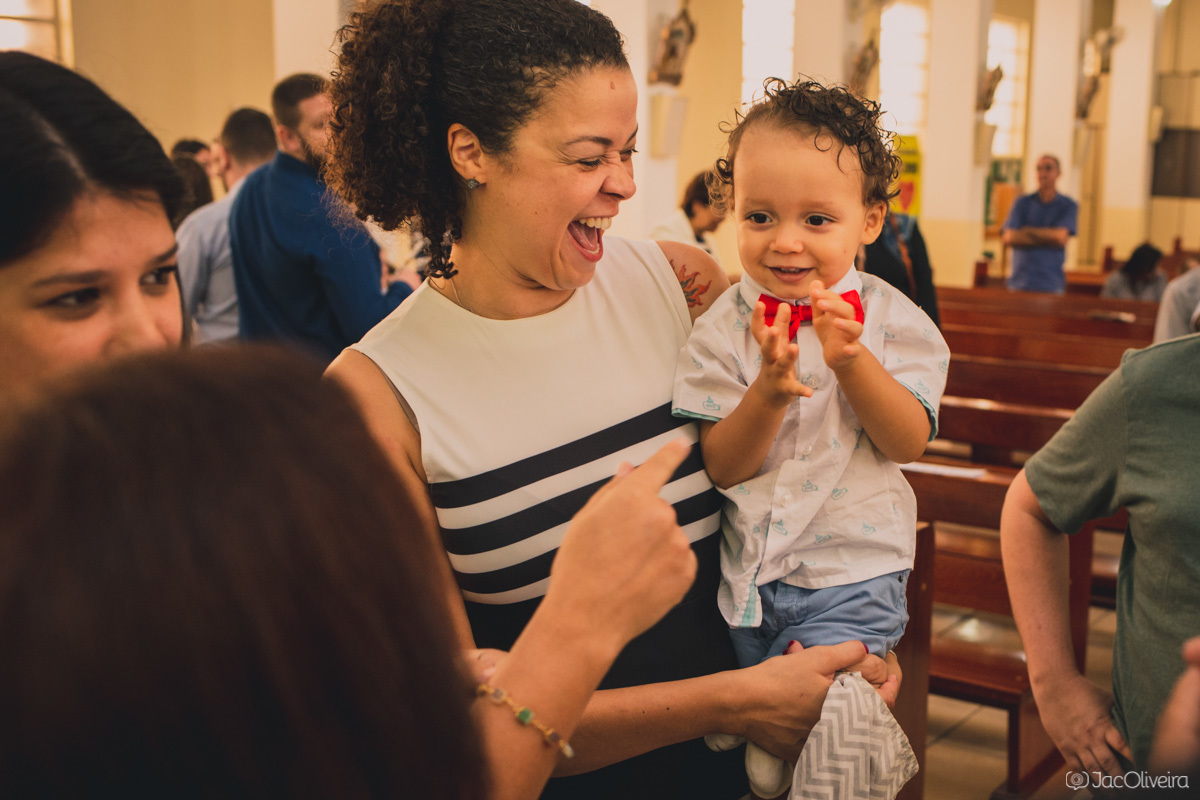 fotografia mãe e filho no batismo mãe dá gargalhada com filho no colo