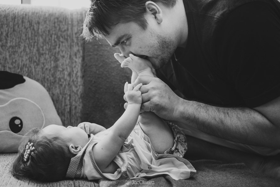 pai beja o pé da filha no sofá da sala ensaio fotografico em casa