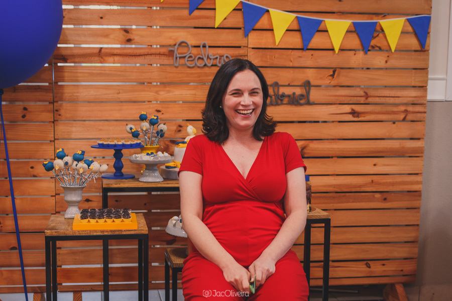 grace rindo no chá de bebê dos gemeos pedro e gabriel com fundo decorado por bandeirolas amarelas e azuis