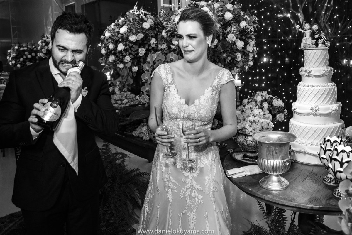 uma foto divertida e inusitada dos noivos abrindo o champanhe durante o brinde na mesa do bolo, a festa de casamento foino Rasen eventos campinas sp