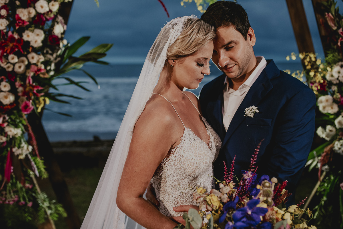 a fotografia espontânea dos noivos que se casaram na praia do litoral de sp com o arco enfeitado de flores bem colorido na decoraçnao do casamento em sp 