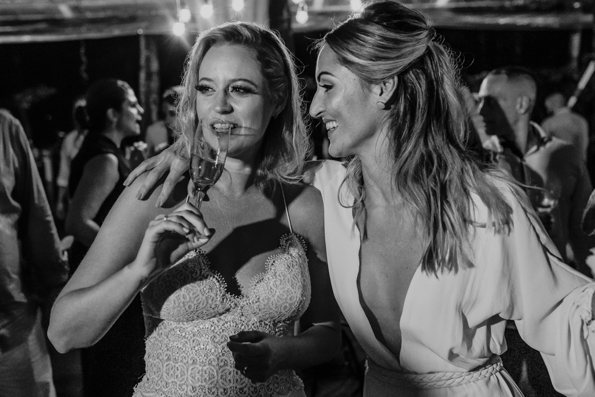 noiva em seu momento mais espontâneo traduzindo sua personalidade nas fotografias de casamento com sua irmã em sua festa de casamento na praia realizado com pé na areia no litoral de sp 