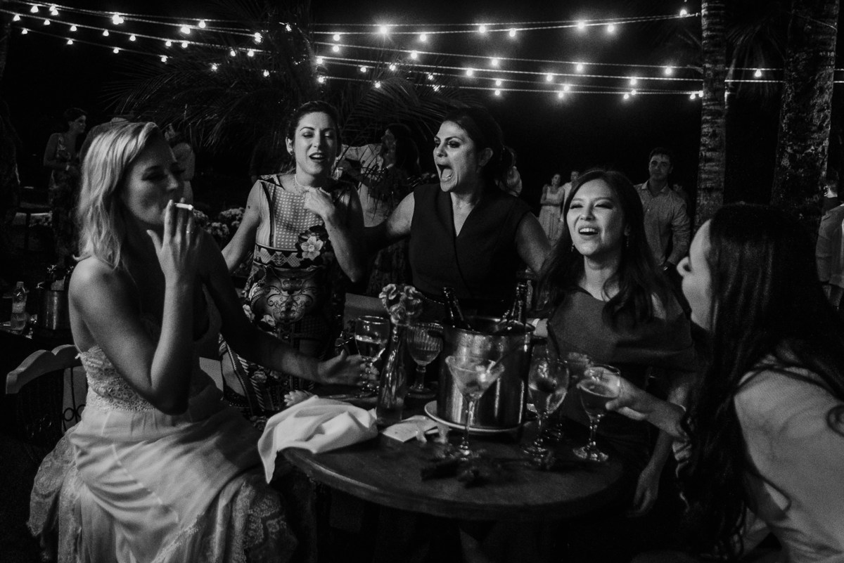 a noiva fumando seu cigarro com toda sua atenticidade junto com as madrinhas e amigas, isso não é uma fotografia clássica, mas sim verdadeira fotografia documental de casamento