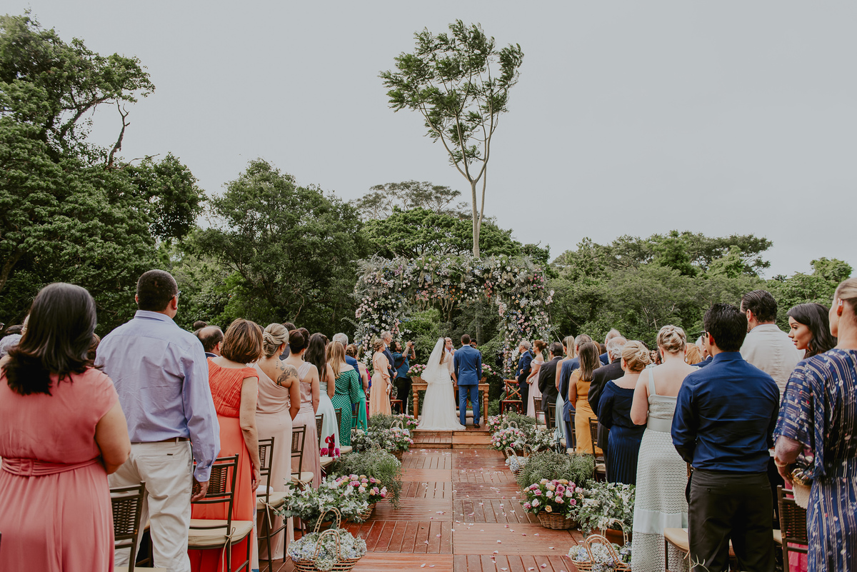 uma foto classica de casamento na fazenda e no campo. mostra parte dos convidados e os noivos de costas no altar. fotografia documental de casamento por daniel okuyama melhor fotografo de casamento do brasil