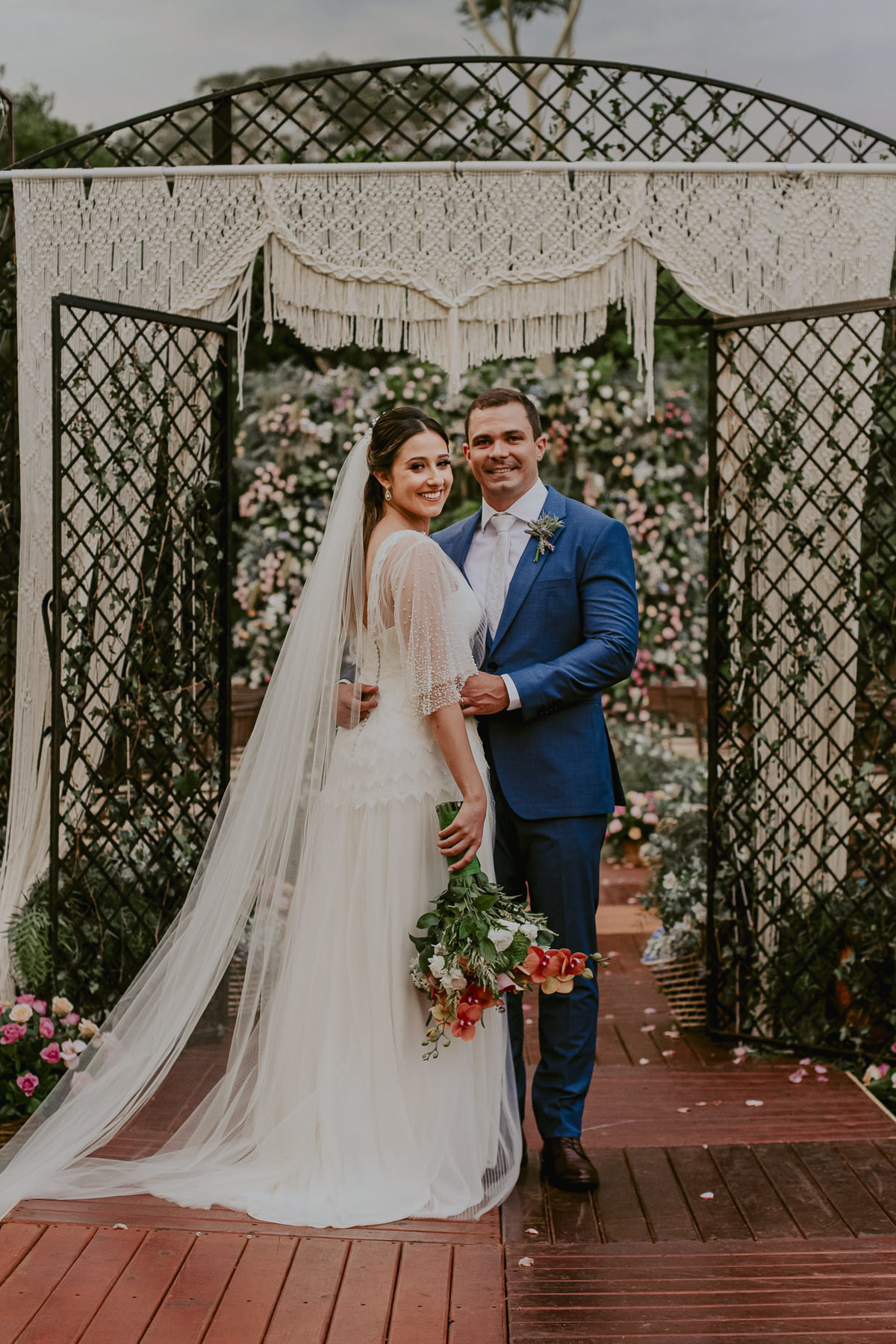 os noivos sorrindo felicidade para as fotos protocolares do casamento ao ar livre. o venstido da noiva pela estilista emanuelle junqueira e o noivo de traje azul