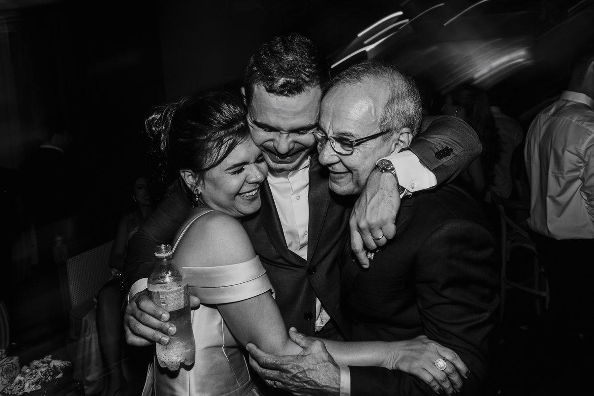 o abraço dos noivos com seus pais durante a animação da festa do casamento em foto divertida 