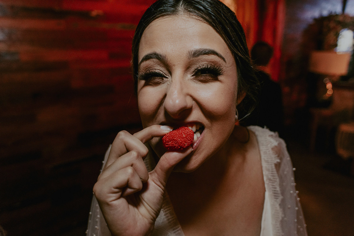 a noiva comendo um doce na festa do seu casamento com expressão engraçada e diverdita