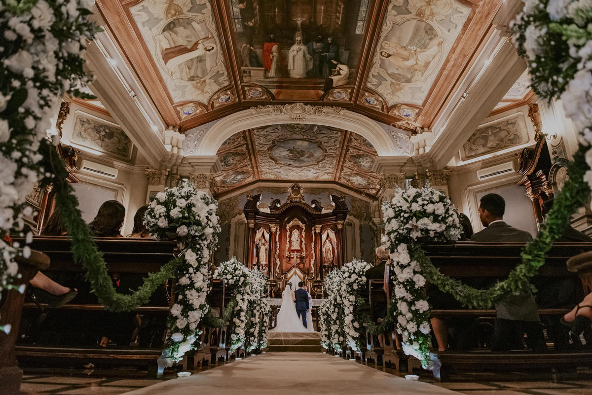 foto classica do casamento os noivos de costa no altar durante a realizacao da cerimoia de casamento realizada na capela da pu igreja imaculada coração de maria capela da puc SP