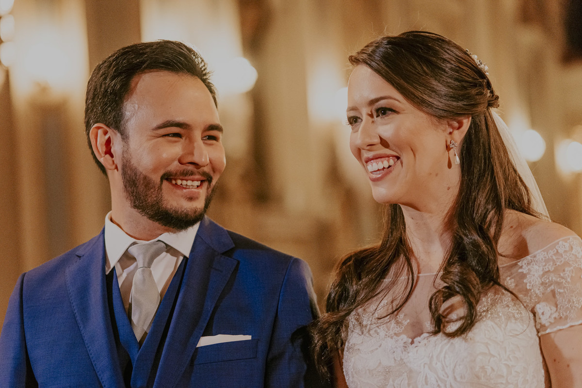 a expressão de amor dos noivos, sorrindo com as palavras do padre que celebra esse lindo casamento na capela da puc sp