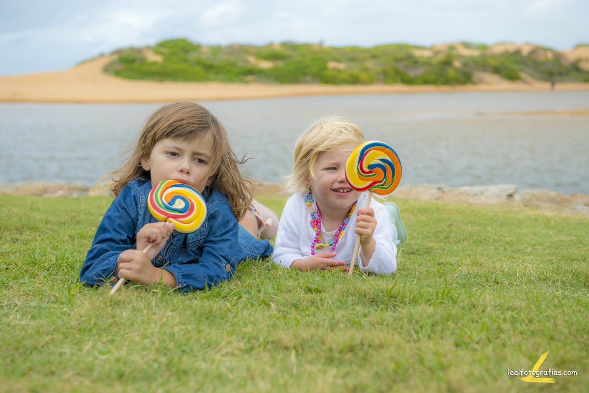 Foto de duas Irmas deitadas na grama com pirulito colorido
