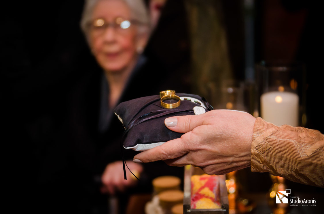 Foto das alianças com a vó do noivo ao fundo