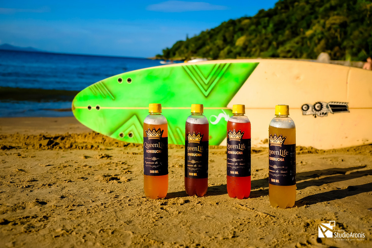 Fotografia de Produtos - Kombuchas - Espumante da Saúde - Balneário Camboriú - Santa Catarina - Prancha de Surf - praia - mar - foto conceito - areia - taça - espumante - fotos com estilo