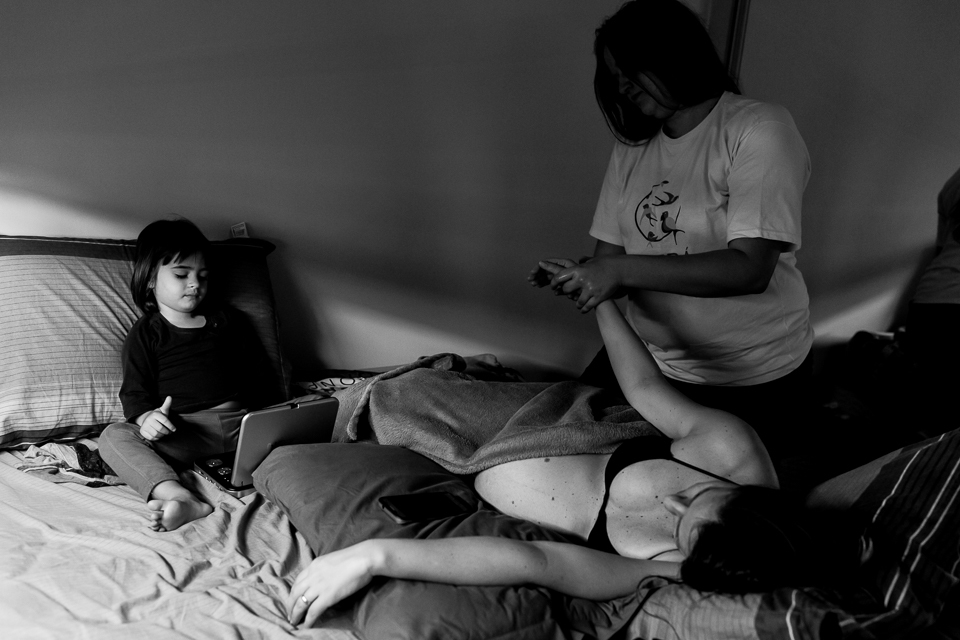 Filha no tablet enquanto a doula faz massagem na mãe gestante a espera de parto natural 